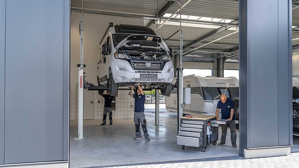 Drei Männer arbeiten unter Hebebühne an Wohnwagen